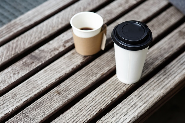 Two cups of coffee to-go stand on wooden bench 