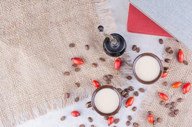 Two cups of coffee with beans and rosehips on burlap.