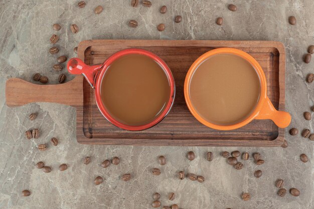 Two cups of coffee on wooden board with coffee beans