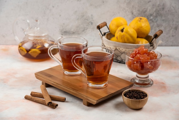 Two cups of hot tea and cinnamon sticks on wooden board. 