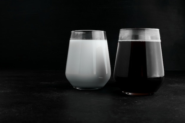 Две чашки молока и темного эспрессо на черном фоне.