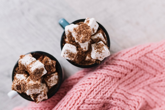 Two cups with marshmallows and knitted scarf