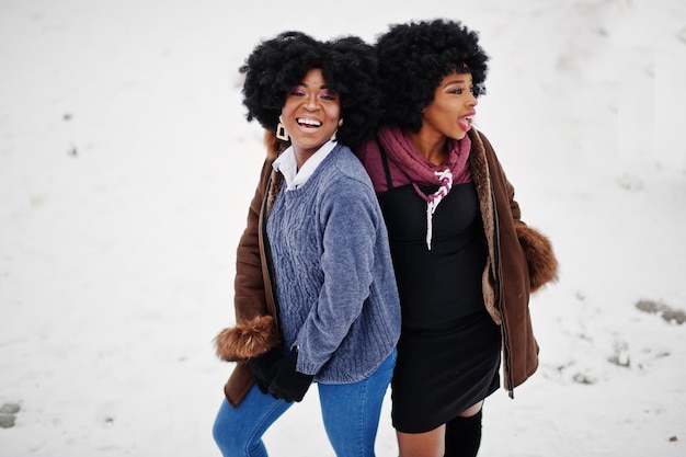Two curly hair african american woman wear on sheepskin coat and gloves posed at winter day