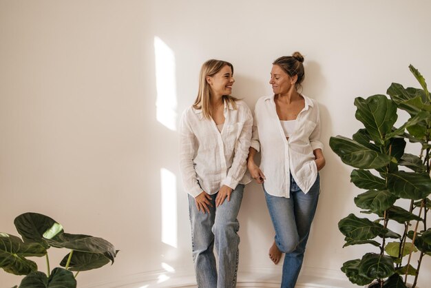 Две милые кавказские молодые женщины в рубашке и джинсах смотрят друг на друга, позируя на белом фоне. Концепция человеческих эмоций, мимики