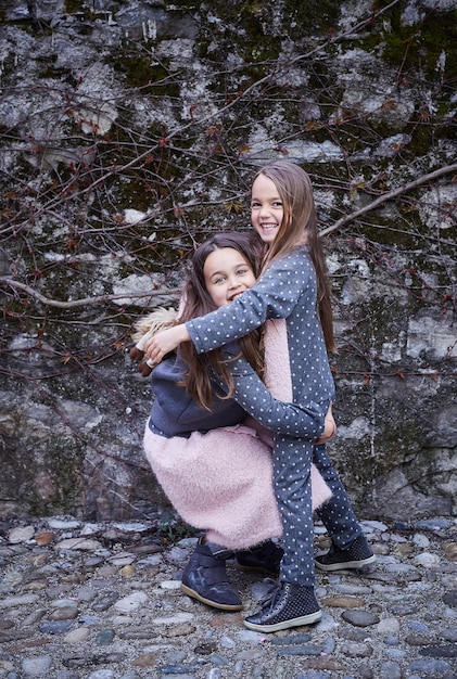 Two cute girlfriends hugging each other over grey stone background.