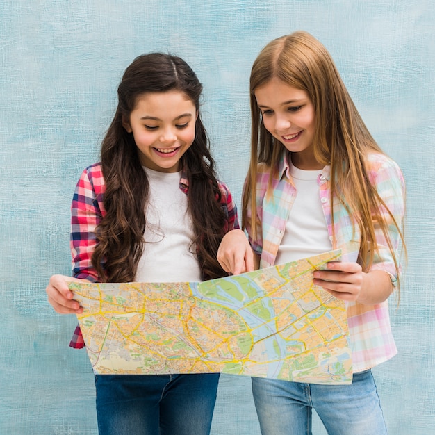 Due ragazze carine in piedi contro il muro dipinto blu alla ricerca nella mappa