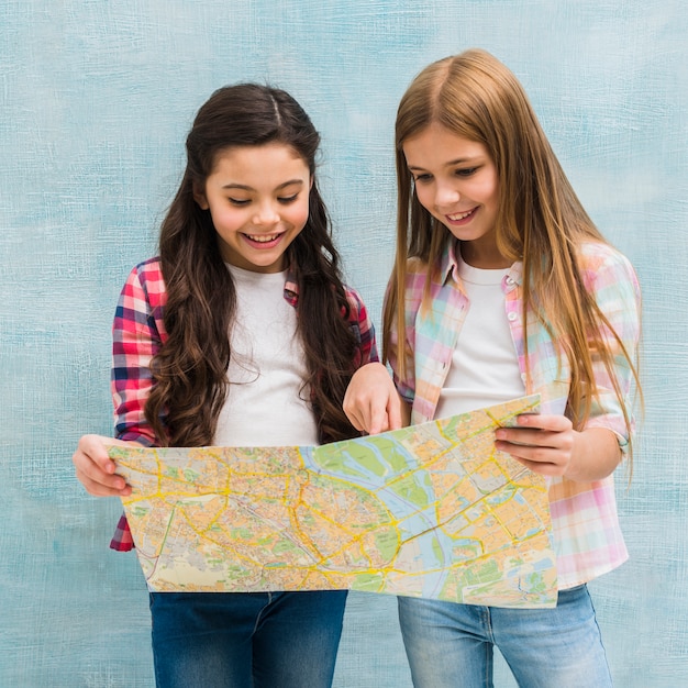 Free photo two cute girls standing against the blue painted wall searching in the map