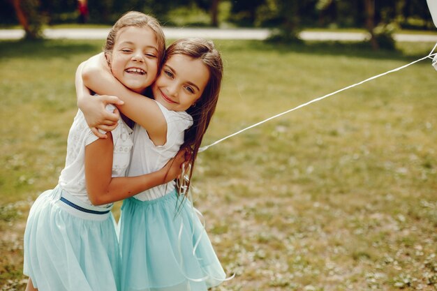 白いTシャツと青いスカートで2人のかわいい女の子が風船で夏の公園で遊ぶ