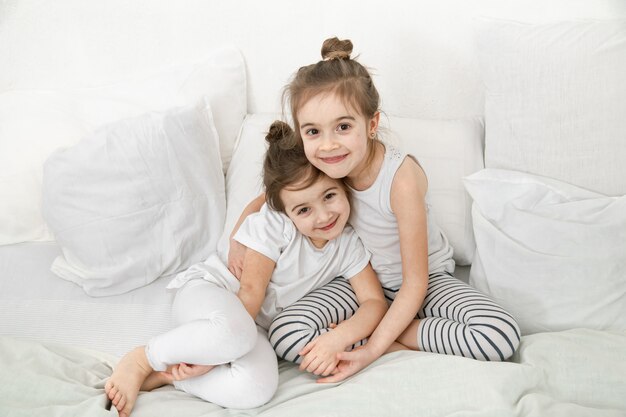 Two cute little sister girls are cuddling on the bed in the bedroom.