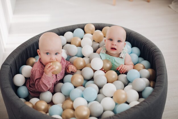 Two cute little toddler posing sitting in bucket with colorful balls having fun. Active children playing together relaxing have positive emotion full shot