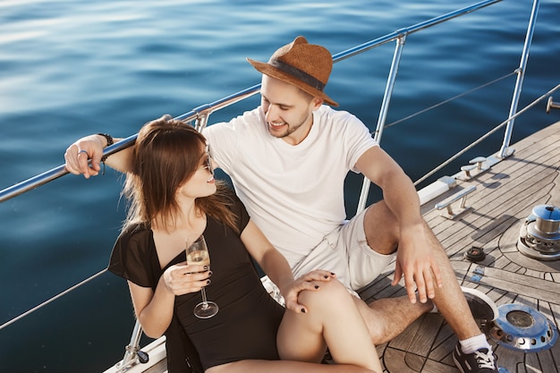 Two cute people in relationship hanging out on yacht, sitting on floor and talking while travelling to island with friends. Couple in love traveled abroad to feel carefree and enjoy each other