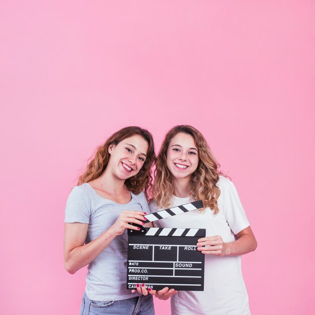 Two cute sister holding clapper in hands against pink backdrop