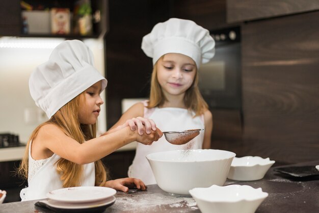 Две милые сестры просеивают какао-порошок через ситечко на кухне
