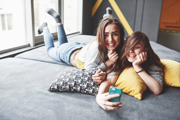 Two cute smiling twins sisters holding smartphone and making selfie.