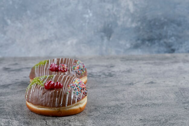 Two delicious chocolate sprinkles donuts on marble surface.