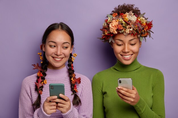 Две разные женщины используют мобильный телефон с декоративными осенними листьями в головах