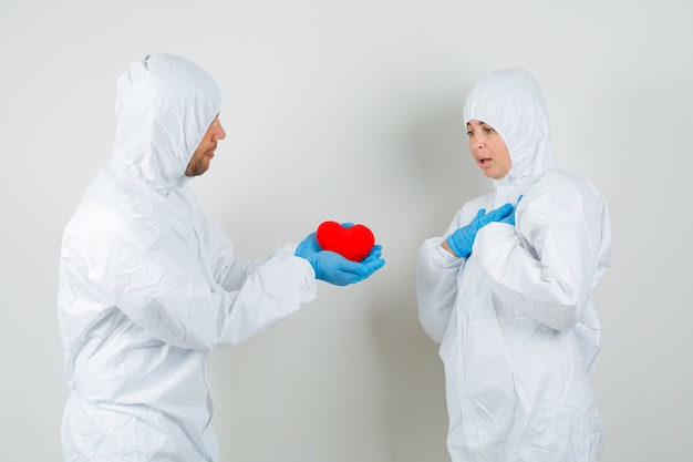 Два врача, дающие друг другу красное сердце в защитном костюме