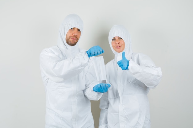 Two doctors holding medical mask and showing thumb up in protective suits