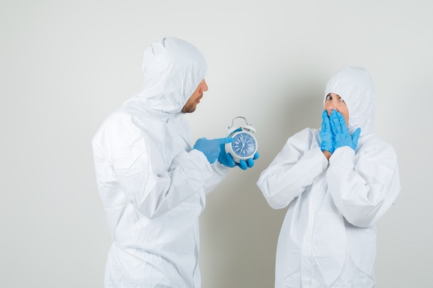 Two doctors pointing at alarm clock in protective suits