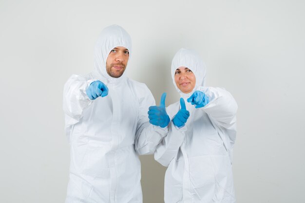 Two doctors pointing at camera and showing thumb up in protective suits