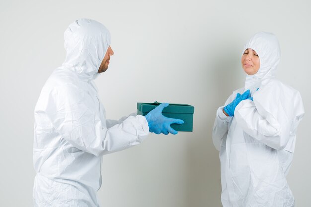 Two doctors in protective suit, gloves giving present box to each other and looking lovely.