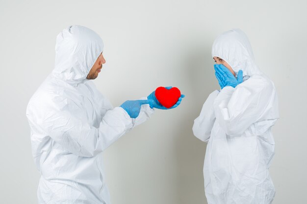 Two doctors in protective suit, gloves giving red heart to each other