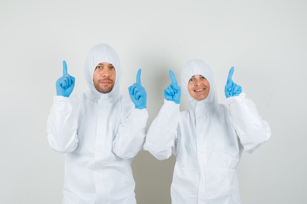 Foto gratuita due medici in tute protettive, guanti che puntano il dito verso l'alto e che sembrano felici