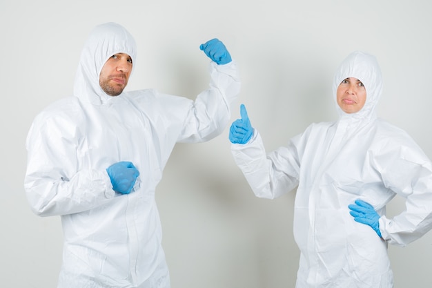 Two doctors in protective suits, gloves showing muscles with thumb up and looking confident