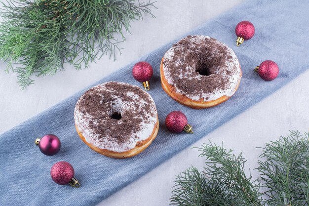 Two donuts and christmas decorations on a folded tablecloth on white surface