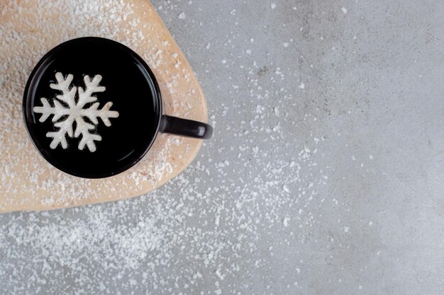 Two donuts and a cup of tea with a snowflake decoration, on a board with sprinkled coconut powder on marble table.