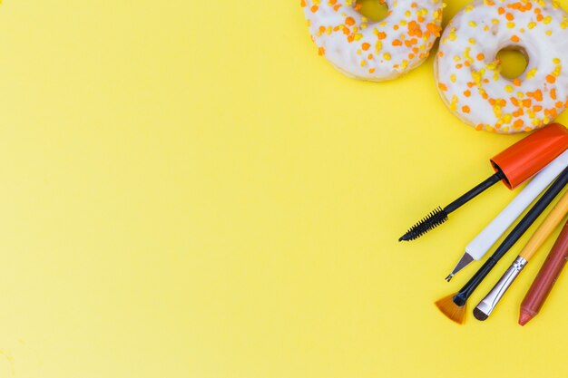 Two donuts; makeup brush; lipstick; mascara and cuticle on yellow background