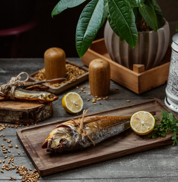 two dried smoked fishes served on wooden board with lemon and parsley