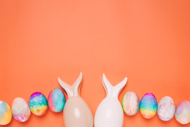 Две пасхальные яйца с ухом кроликов на оранжевом фоне
