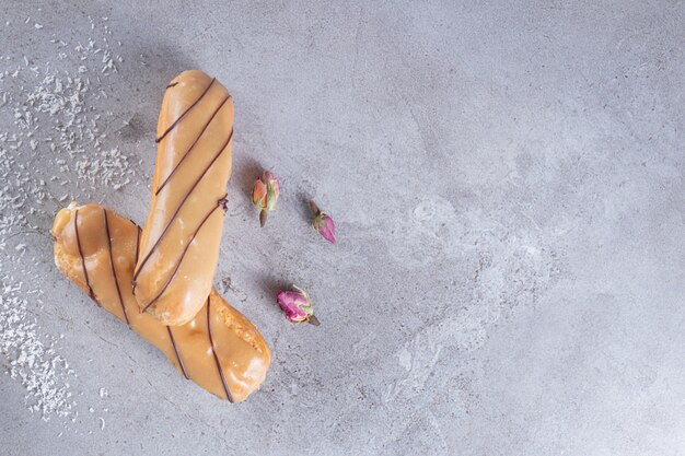 Two eclairs with caramel fillings and roses on stone background. 