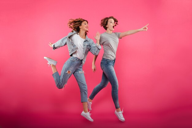 Two emotional ladies friends jumping and pointing.