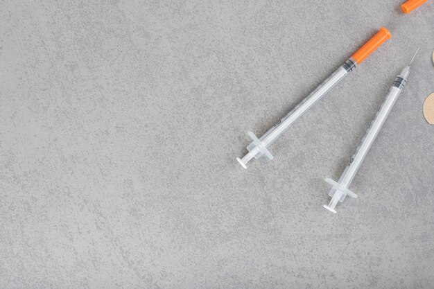 Two empty syringes with three plasters on a gray surface