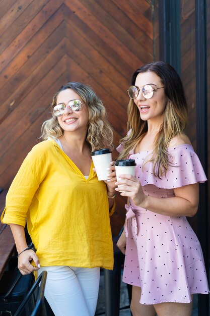 Free photo two excited stylish girlfriends drinking coffee in cafe