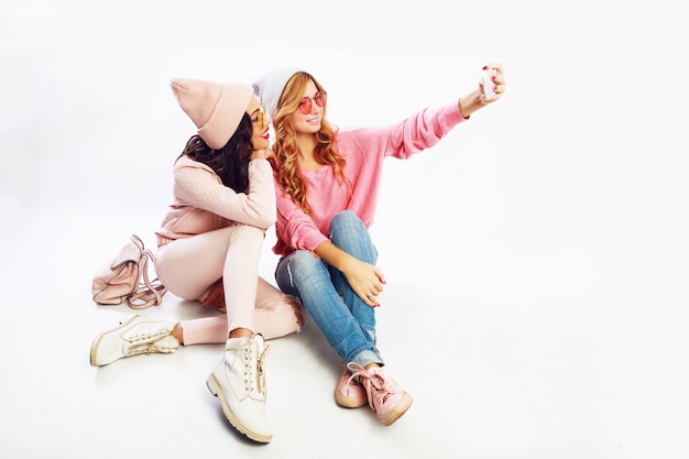 Free photo two fashionable miling girls making self portrait. white background. pink  clothes.