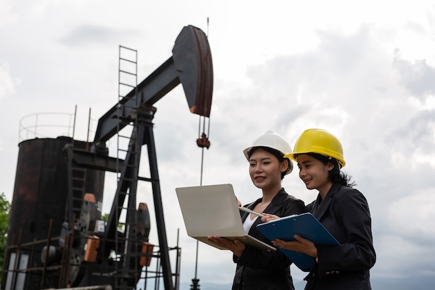 Two female engineers stand beside working oil pumps with a white sky .