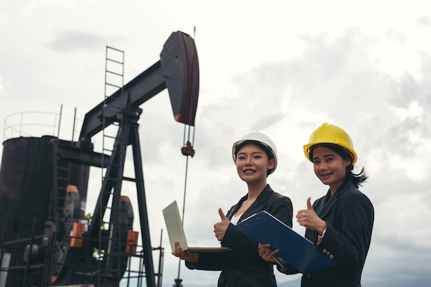 Two female engineers stand beside working oil pumps with a white sky .