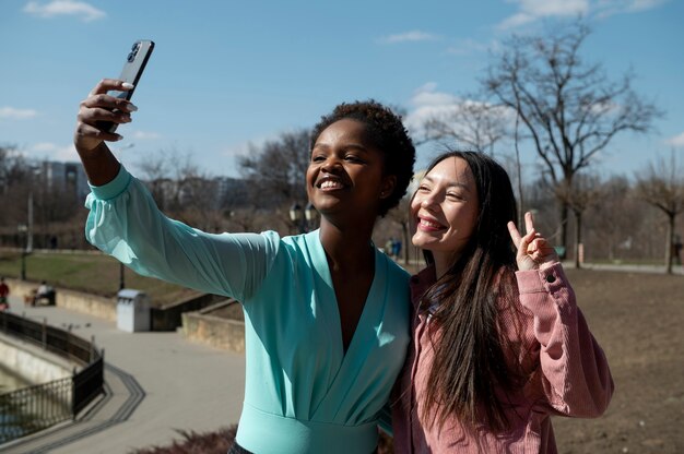 Two female friends celebrating the lifting of face mask restrictions by taking a selfie outdoors