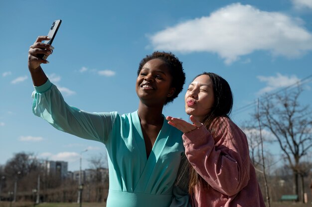 Two female friends celebrating the lifting of face mask restrictions by taking a selfie outdoors