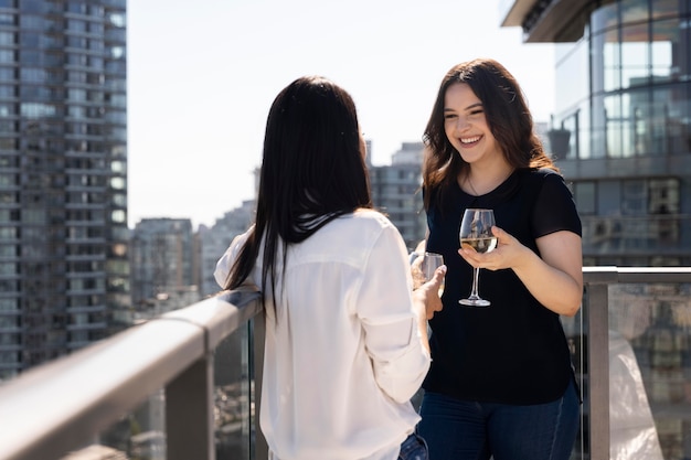 Foto gratuita due amiche conversano e si godono un po' di vino su una terrazza sul tetto