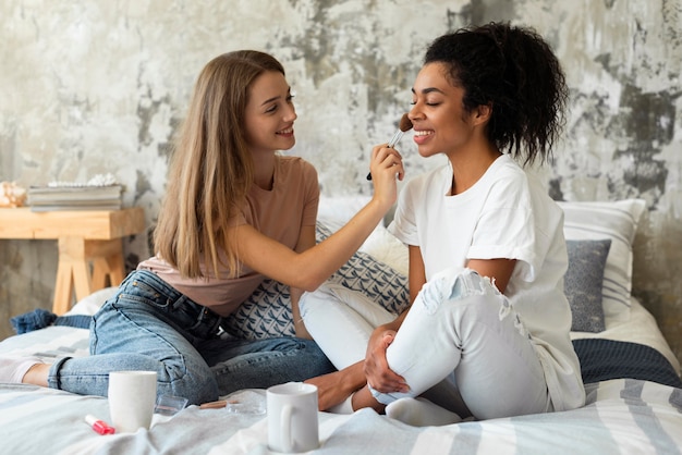 two female friends doing make-up on each other in bed