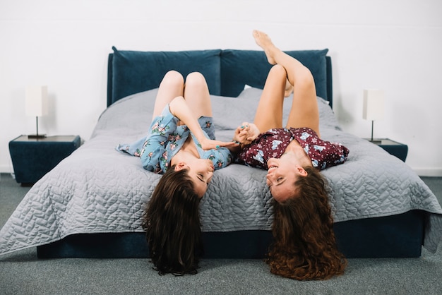 Two female friends having fun while lying on bed