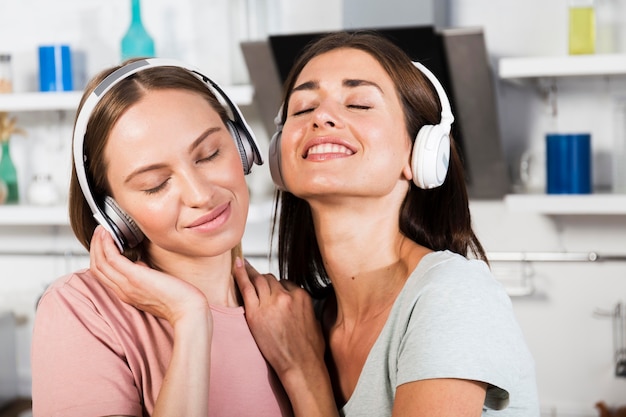 Two female friends at home listening to music on headphones