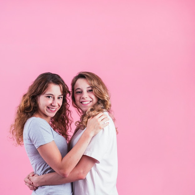 분홍색 배경에 대해 서로 포옹하는 두 여자 친구