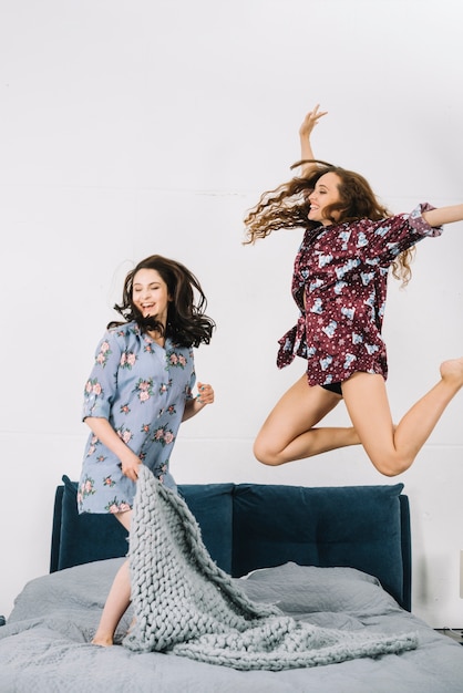 Free photo two female friends jumping on bed in bedroom