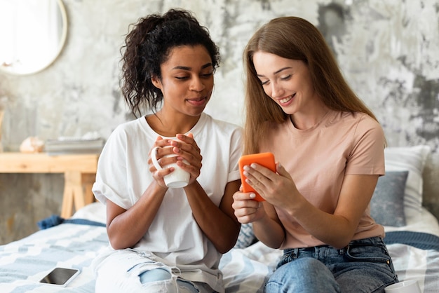 Two female friends looking at smartphone while having a drink