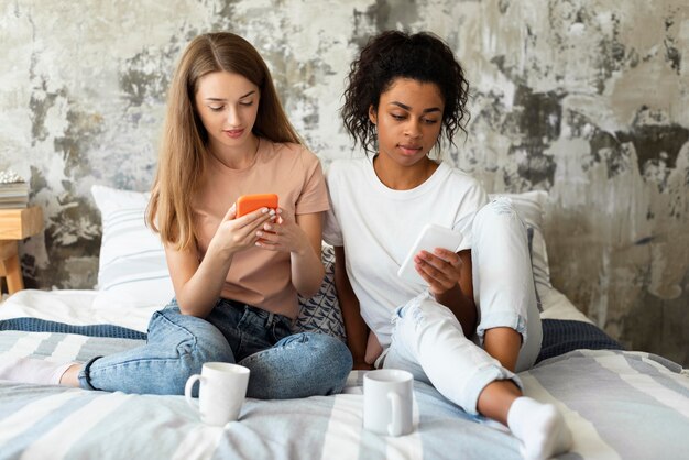 Two female friends looking at smartphones in bed